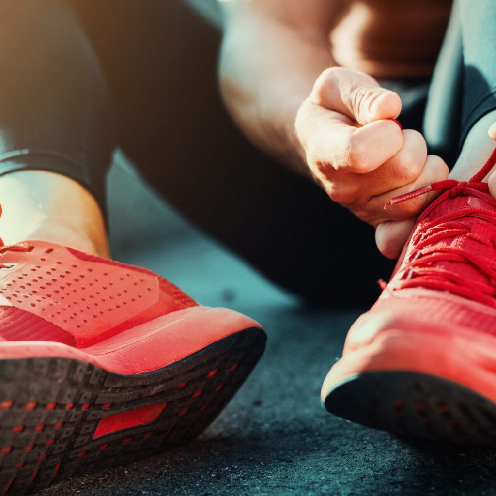 Was kommt Ihnen in den Sinn, wenn Sie an den Monat Januar denken? 13 Eine Person sitzt auf dem Boden und bindet die Schnürsenkel von leuchtend roten Sportschuhen. Der Fokus liegt auf ihren Händen und Schuhen, wobei das Sonnenlicht die Szene beleuchtet.