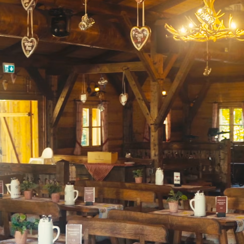 Peter’s Oktoberfest: Tradition trifft auf moderne Gemütlichkeit 8 Ein gemütliches Holzrestaurant mit rustikalen Tischen und Bänken, weißen Krügen als Tafelaufsatz, von der Decke hängenden herzförmigen Dekorationen und warmer Raumbeleuchtung.